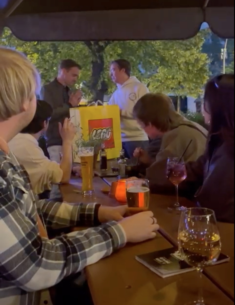 Se muestra la terraza del biergarten en Berlín con uno de los estudiantes entregándome el regalo en la cabecera de la mesa