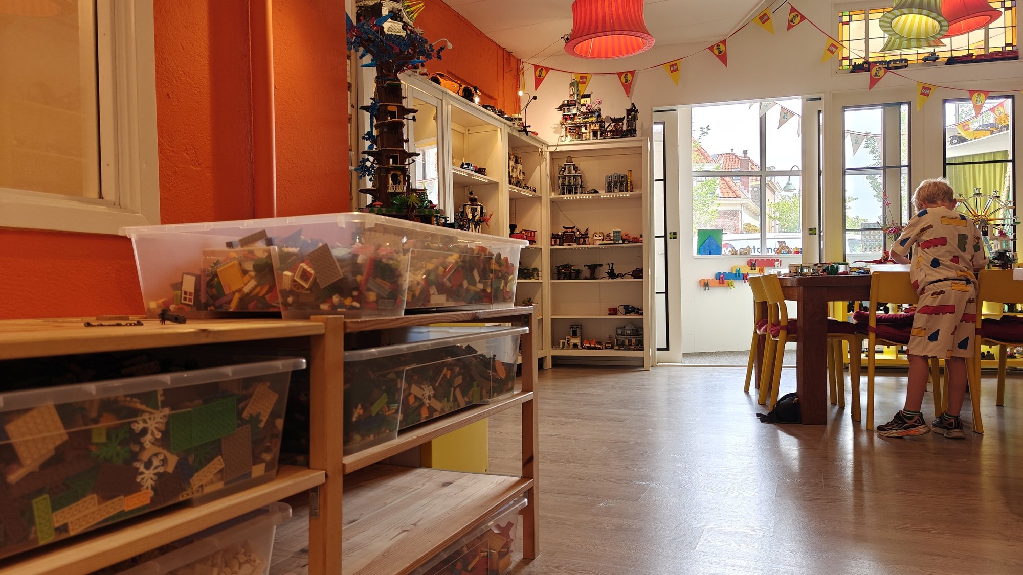 Vue de l'espace de l'atelier avec des créations et des boîtes pleines de LEGO®, à l'arrière-plan mon fils construit à notre table de travail