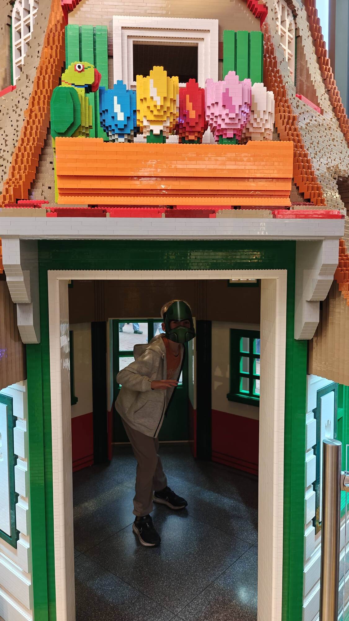 Son standing in a small house built entirely out of LEGO®