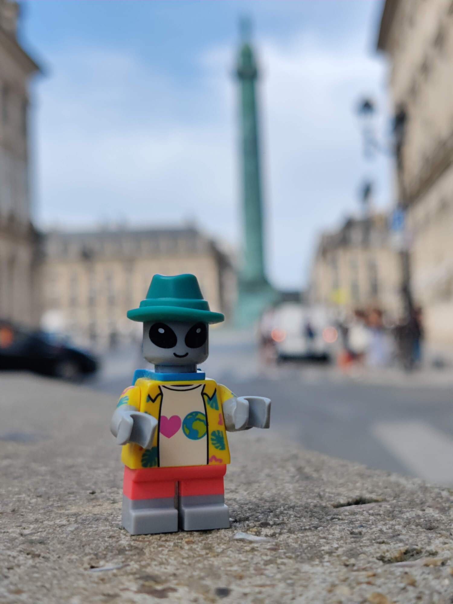 Alien-Minifig steht auf einem Platz mit einigen französischen Gebäuden im Hintergrund