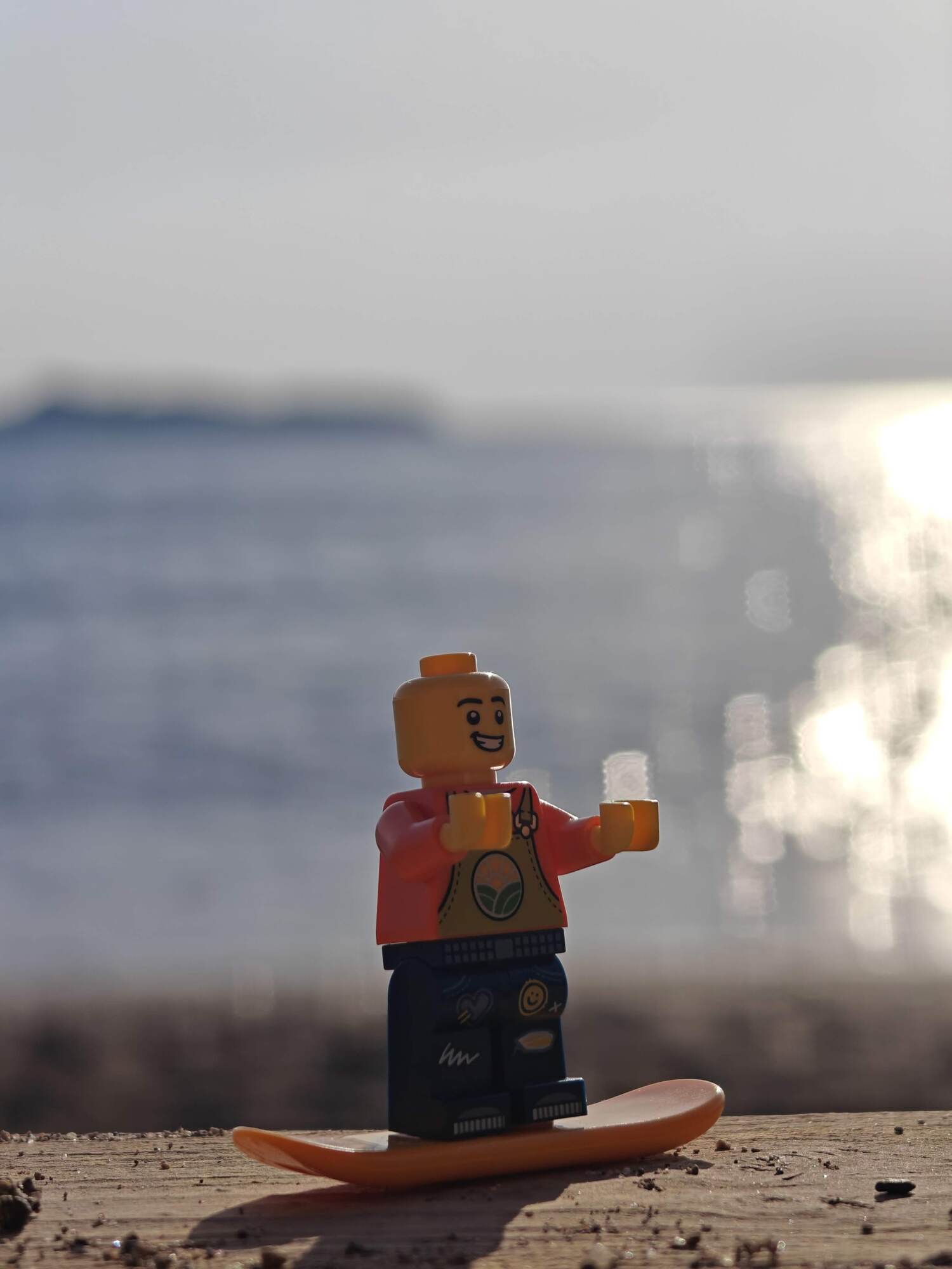 Minifig steht auf einem Surfbrett mit dem Meer im Hintergrund