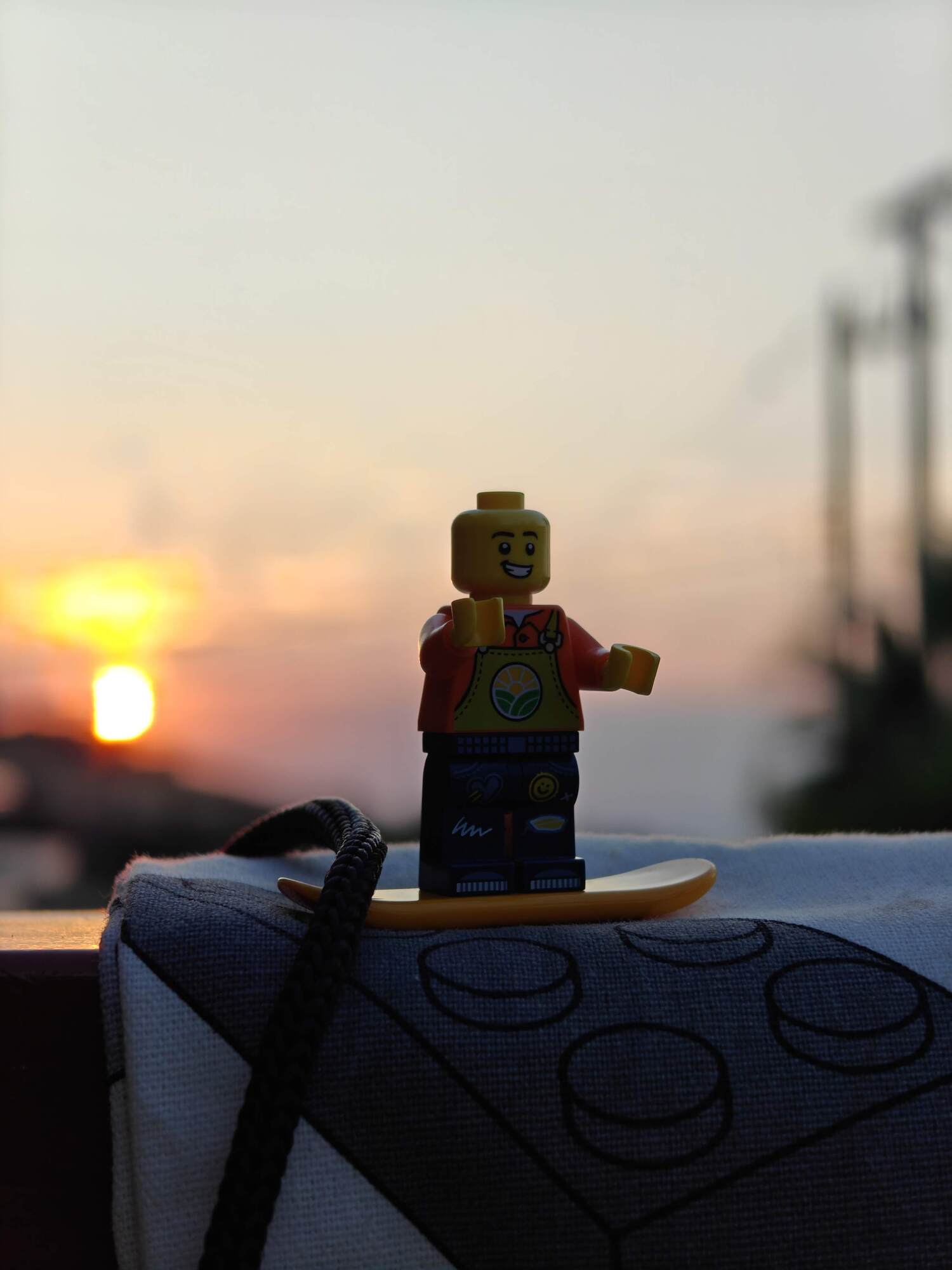 Minifig posiert auf einer LEGO®-Tasche mit dem Sonnenuntergang im Hintergrund